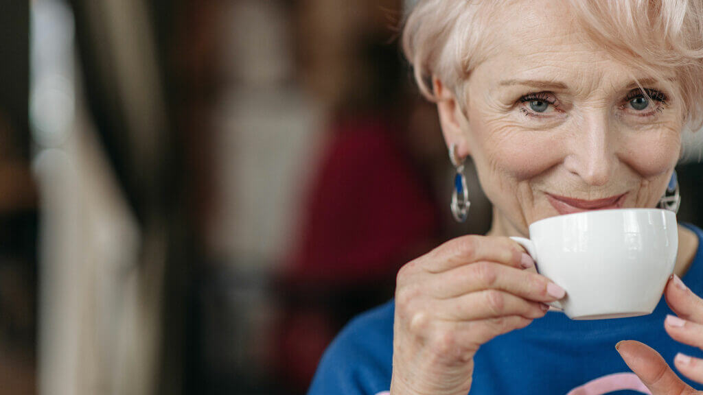 A senior woman drinking tea and smiling.